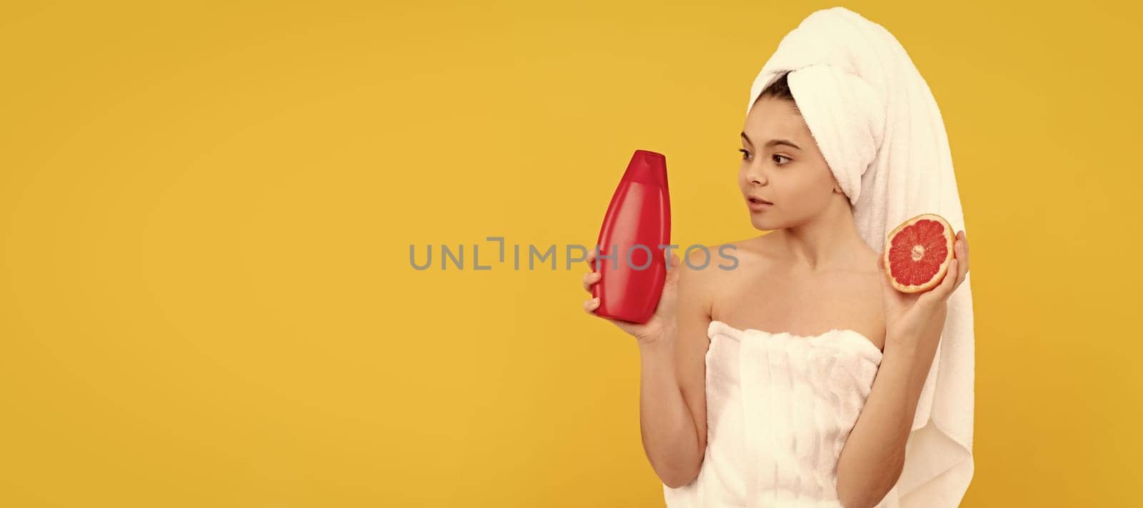 teen kid in towel with grapefruit shampoo bottle on yellow background. Cosmetics and skin care for teenager child, poster design. Beauty kid girl banner with copy space. by RedFoxStudio