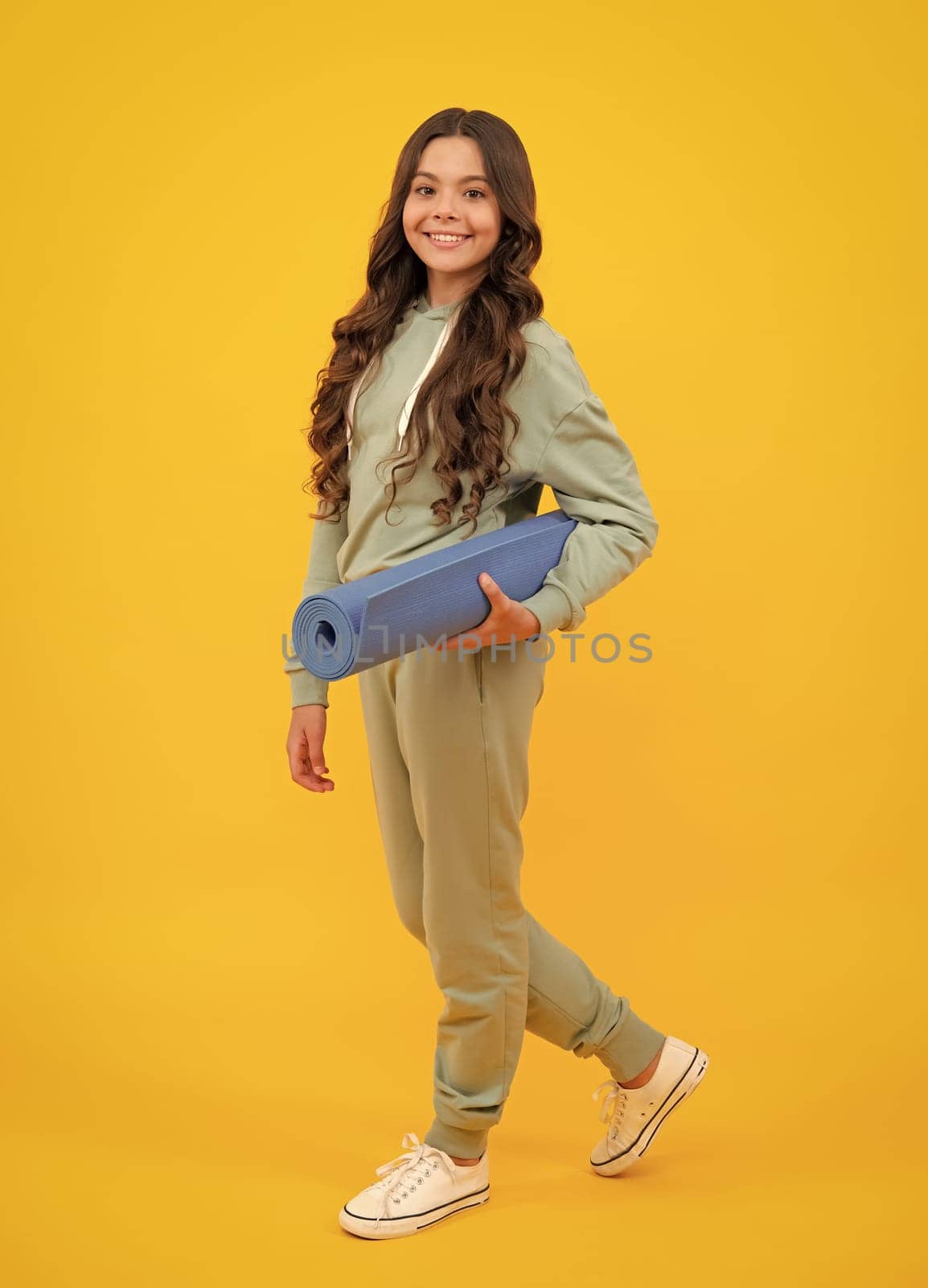 Girl teenager in tracksuit. Happy cute child in a yellow sports suit on a yellow background. Sportswear advertising concept