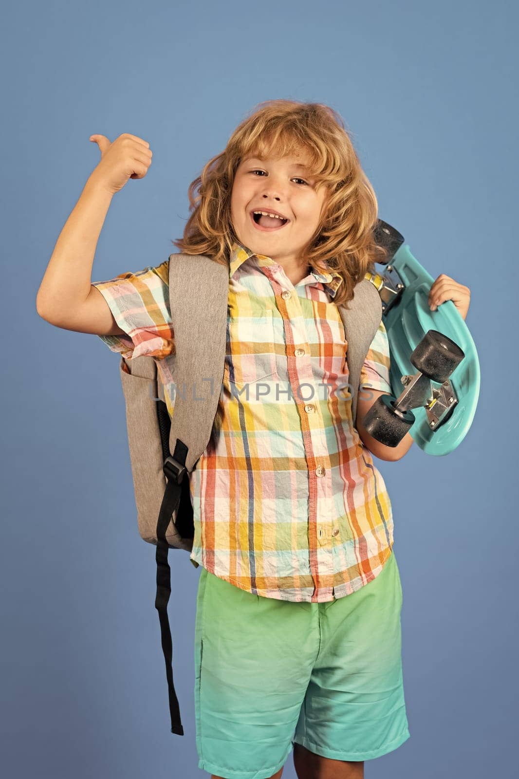 Happy child boy holding skateboard over blue background isolated. Studio portrait of fashion kids