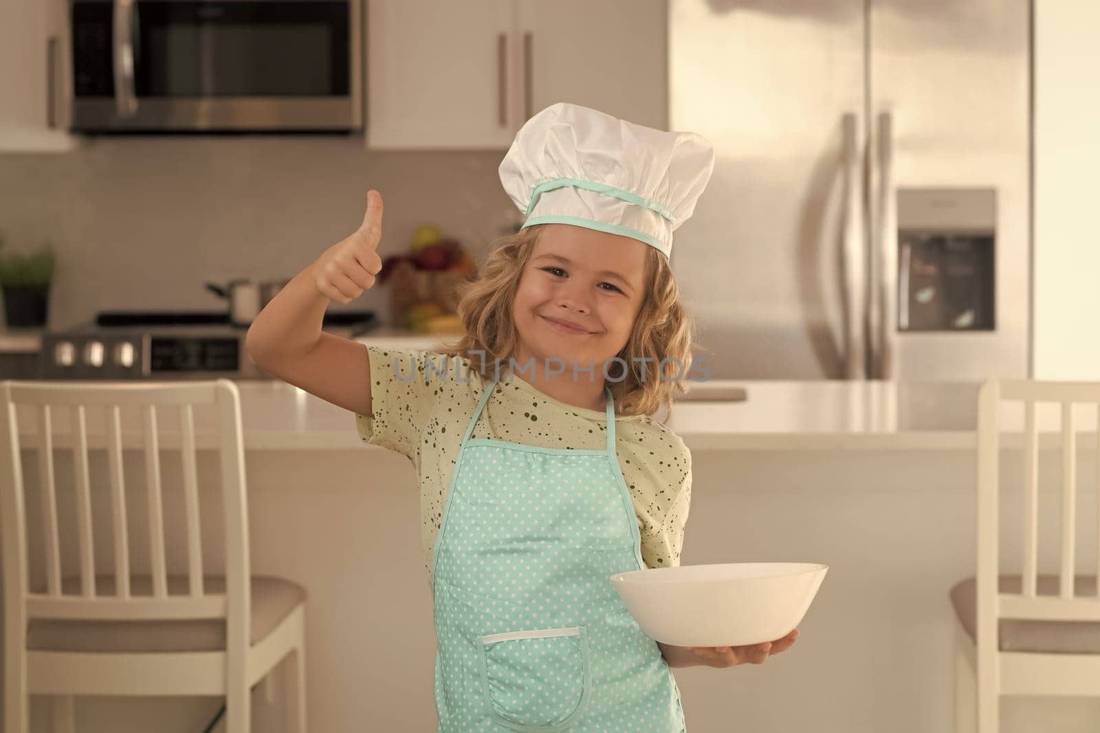 Child chef cook with cooking plate. Child chef cook is learning how to make a cake in the home kitchen. Child making tasty delicious. little boy in chef hat and an apron cooking in the kitchen. by RedFoxStudio