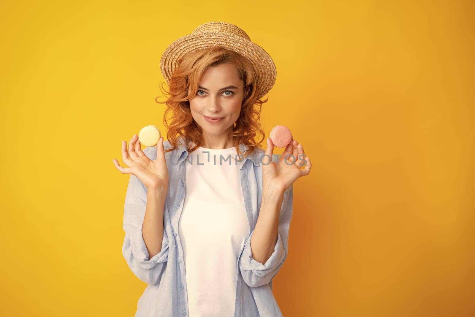 Woman eating a macaroon. Beautiful redhead woman in summer straw hat eating sweet macaroons. French dessert, sweets