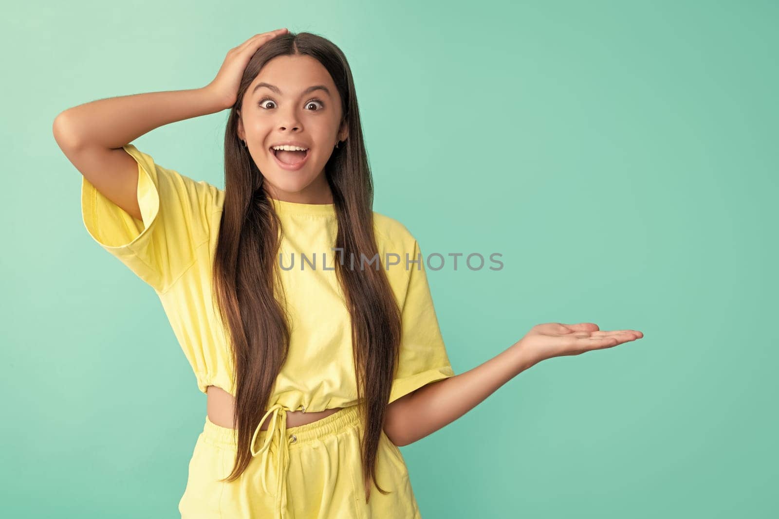 surprised kid presenting product with copy space. beauty and fashion. female fashion model. pretty look of young girl. face portrait of child on blue background. express positive emotions.