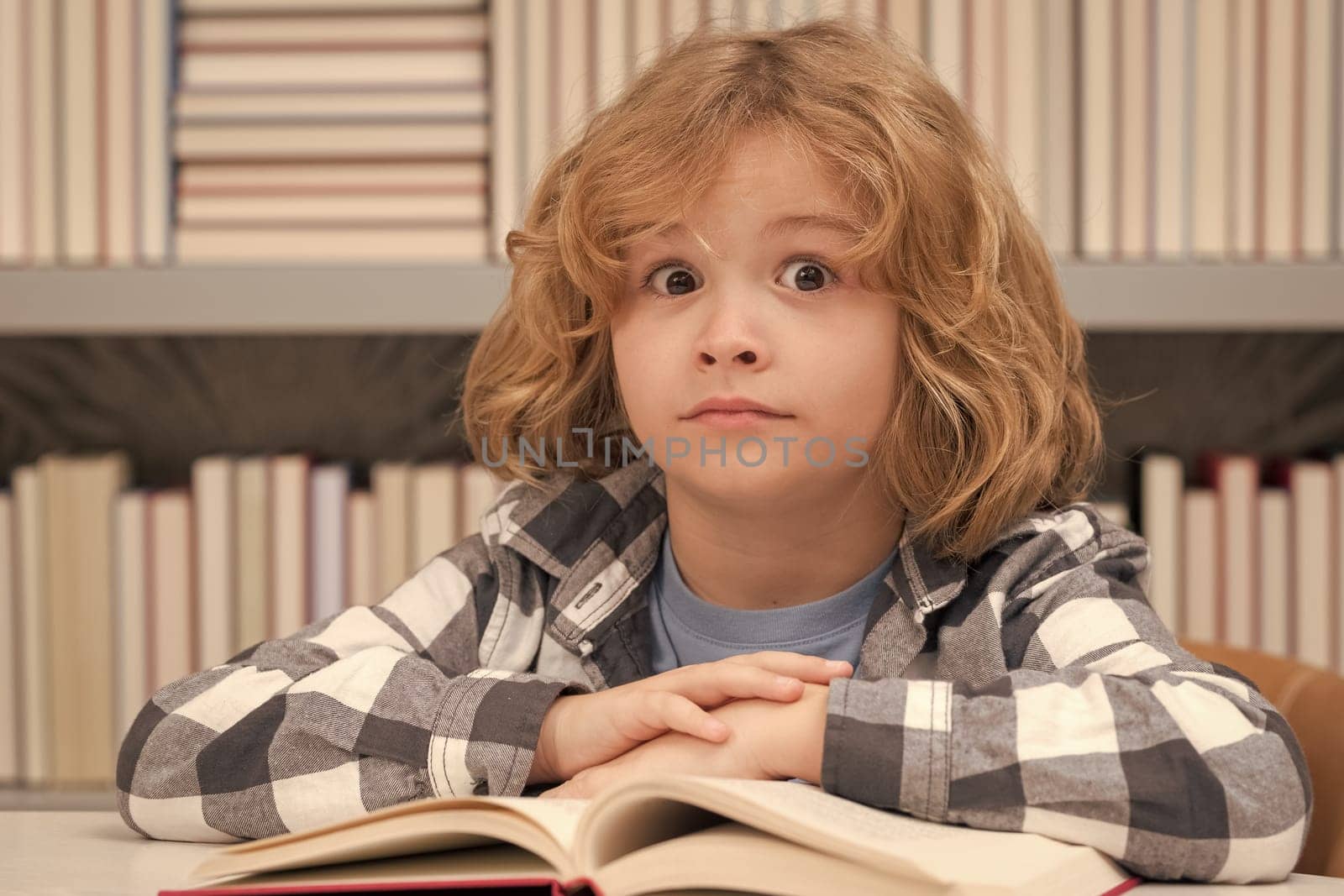 Cute school kid studying in school library. Portrait of child reading in library on background with books