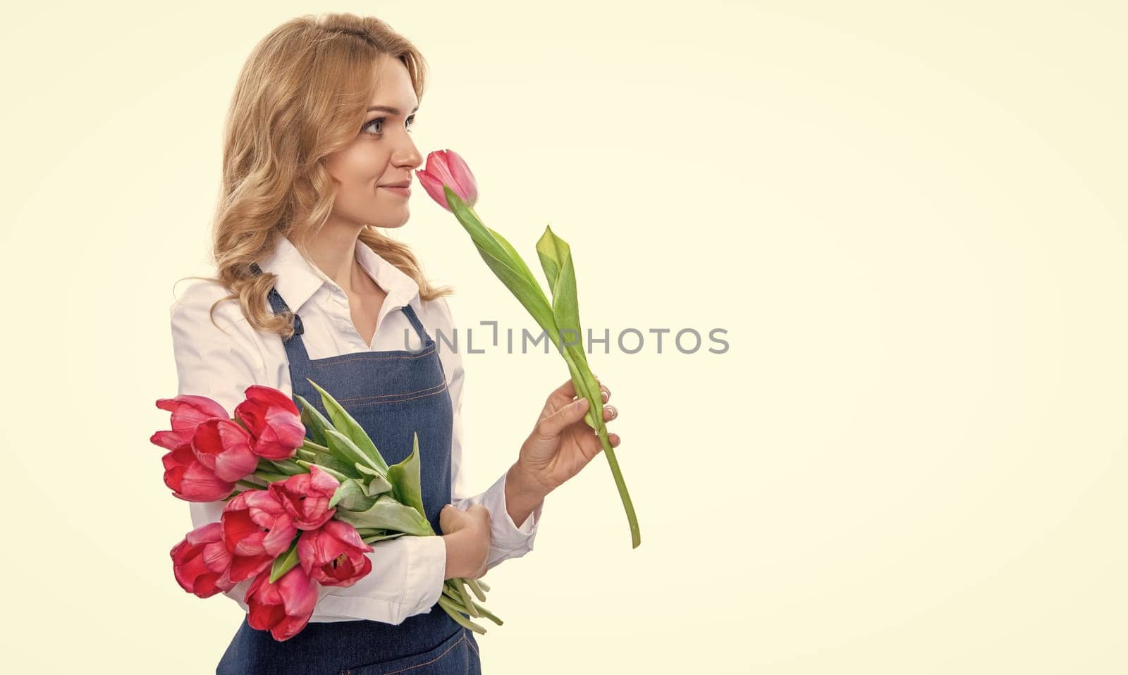 happy young woman in apron smell spring tulip flowers isolated on white background by RedFoxStudio