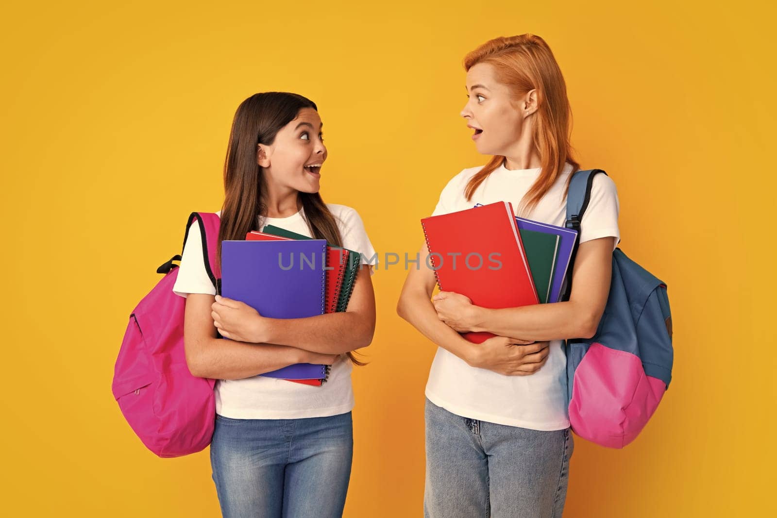 School, learning and education concept. Mother and daughter schoolgirls with school backpack and books ready to learn. Back to school. Mom and child on isolated yellow studio background. by RedFoxStudio