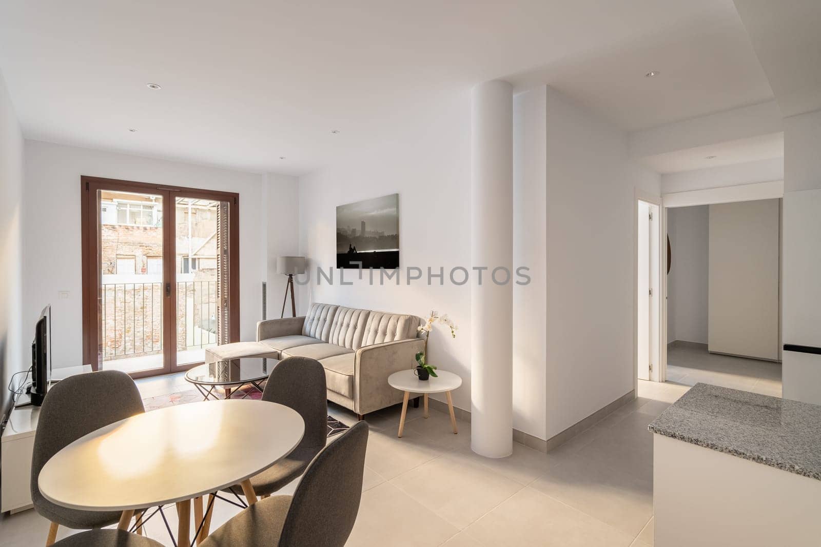 Spacious living-dining room with table and chairs, sofa, table and TV and decorative accessories with panoramic window and access to the balcony. Studio apartment concept.