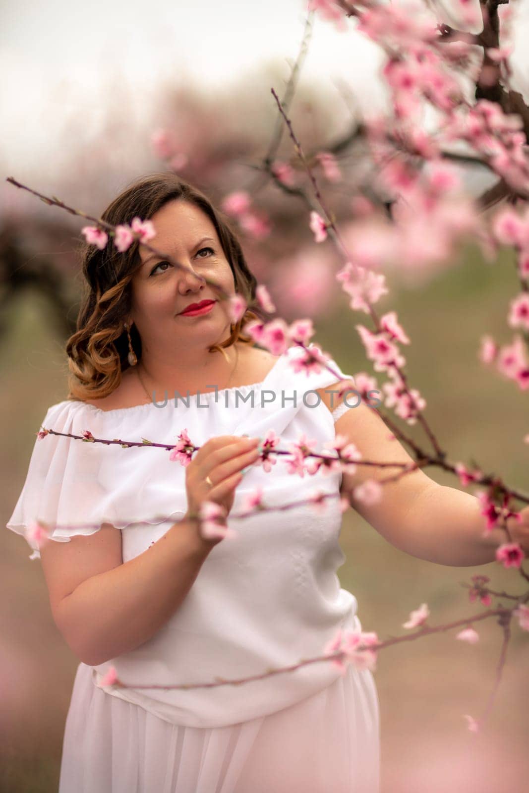 Woman peach blossom. Happy woman in white dress walking in the garden of blossoming peach trees in spring.