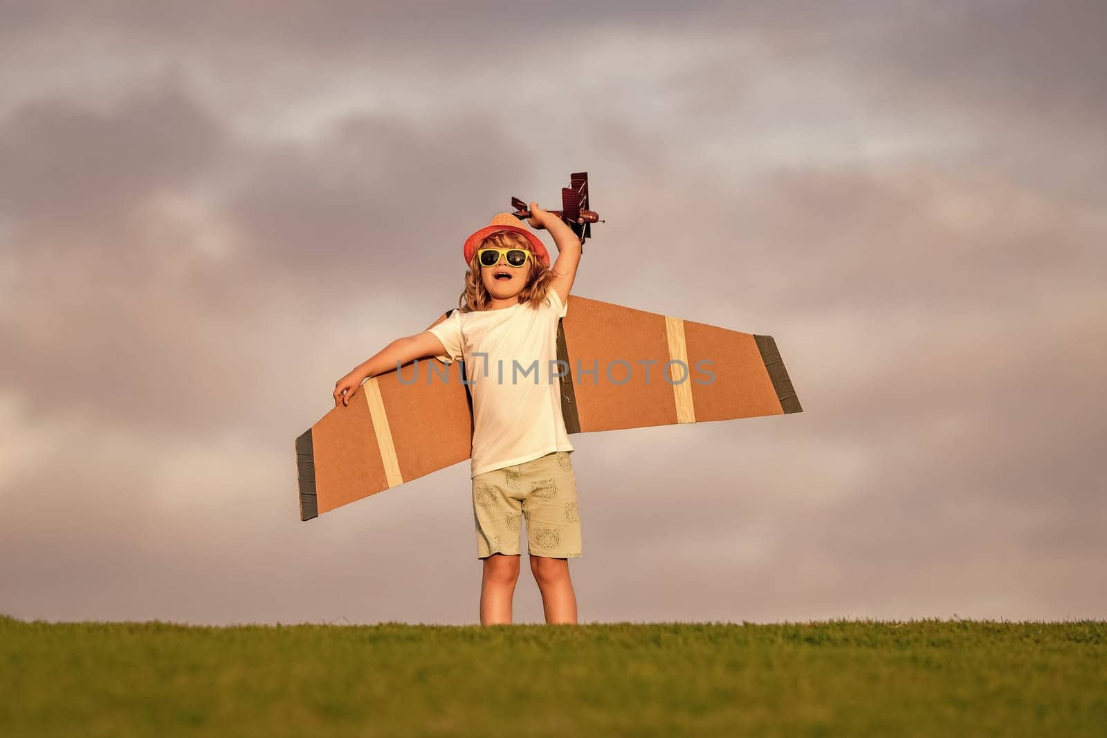 Kid pilot aviator with with paper wings dreams of traveling in summer in park outdoor