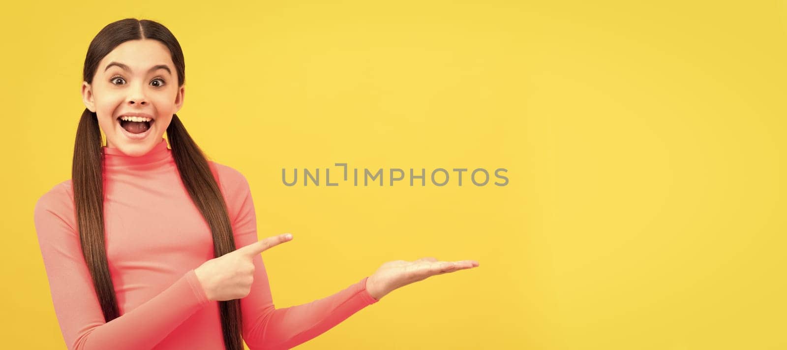 amazed kid pointing finger on copy space on yellow background, shopping sale. Child face, horizontal poster, teenager girl isolated portrait, banner with copy space