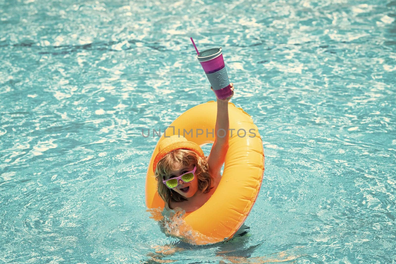 Child in swimming pool on inflatable float ring. Water toy, healthy outdoor sport activity for children. Kids beach fun. Child splashing in summer water pool