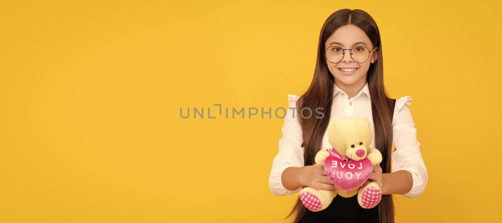 Happy school age kid hold teddy bear with love you heart yellow background, Valentines gift. Banner of child girl with toy, studio portrait, header with copy space. by RedFoxStudio