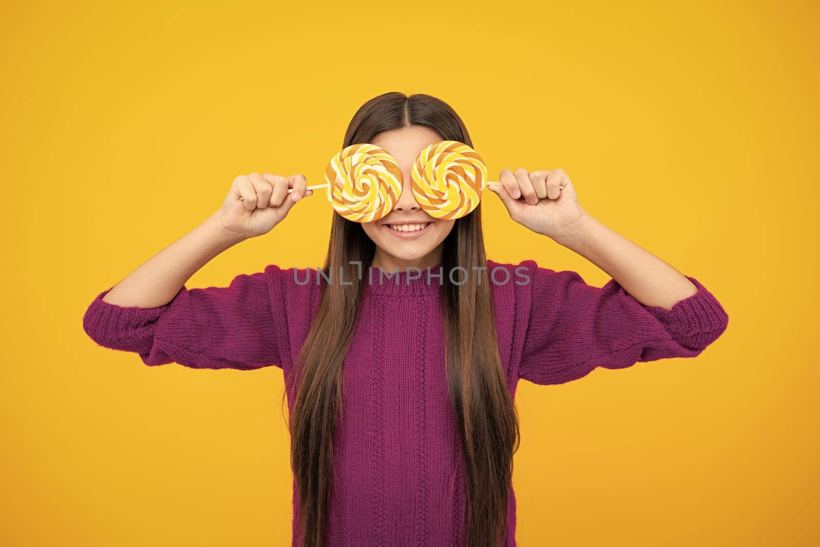 Funny child with lollipop over yellow isolated background. Sweet childhood life. Teen girl with yummy caramel lollipop, candy shop. Teenager with sweet sucker