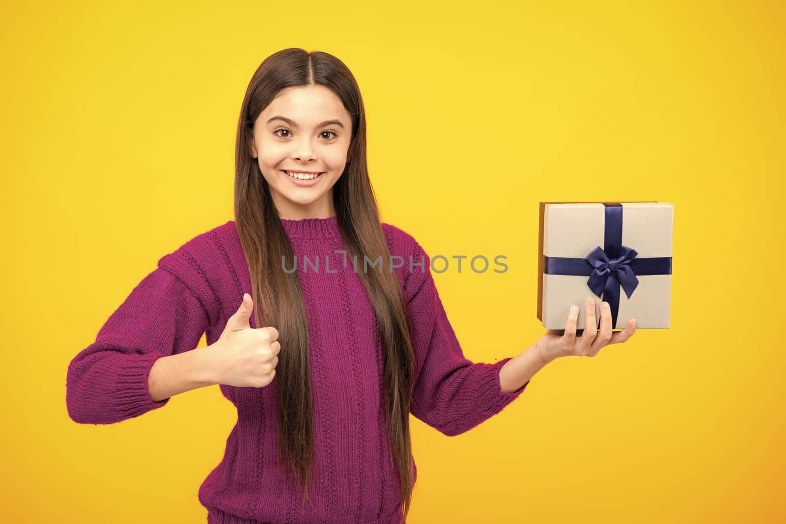 Portrait of a teenager child girl holding present box isolated over yellow studio background. Present, greeting and gifting concept. Birthday holiday concept