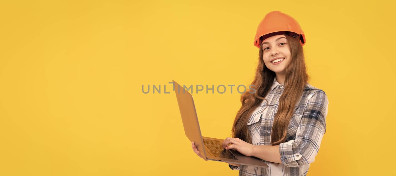 happy teen girl in helmet and checkered shirt using laptop, education online. Child builder in helmet horizontal poster design. Banner header, copy space. by RedFoxStudio