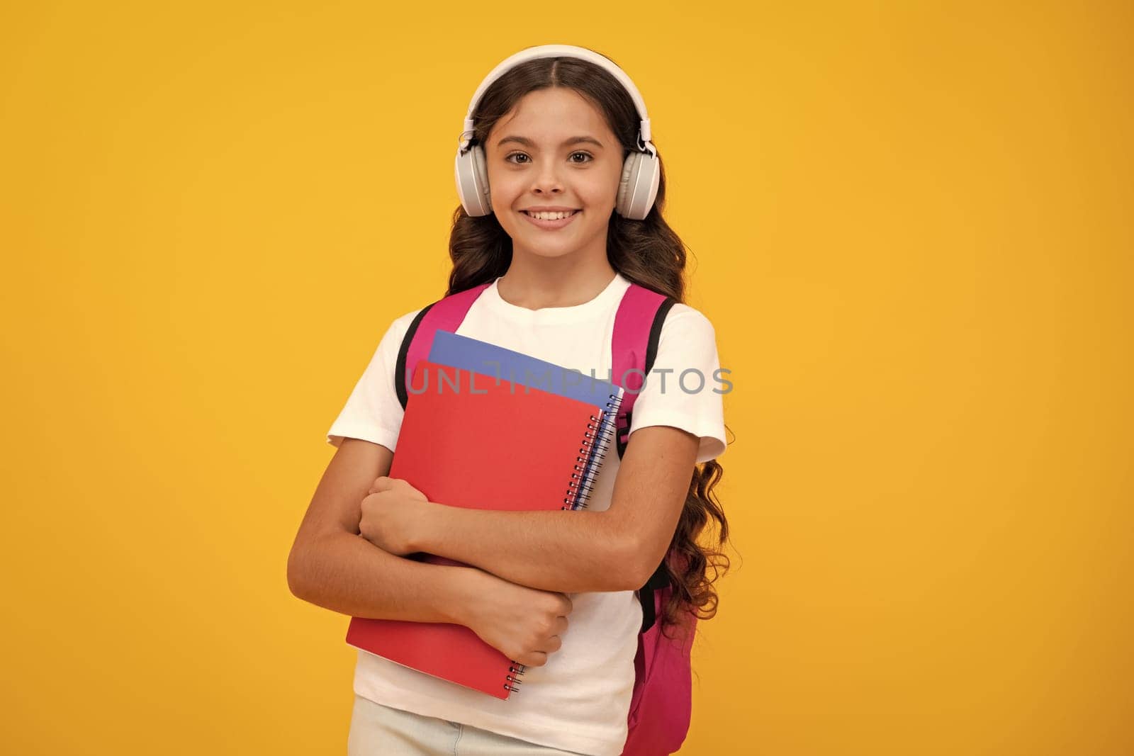 Back to school. Teenager school girl with backpack and headphones hold books ready to learn. School children on isolated yellow studio background. by RedFoxStudio
