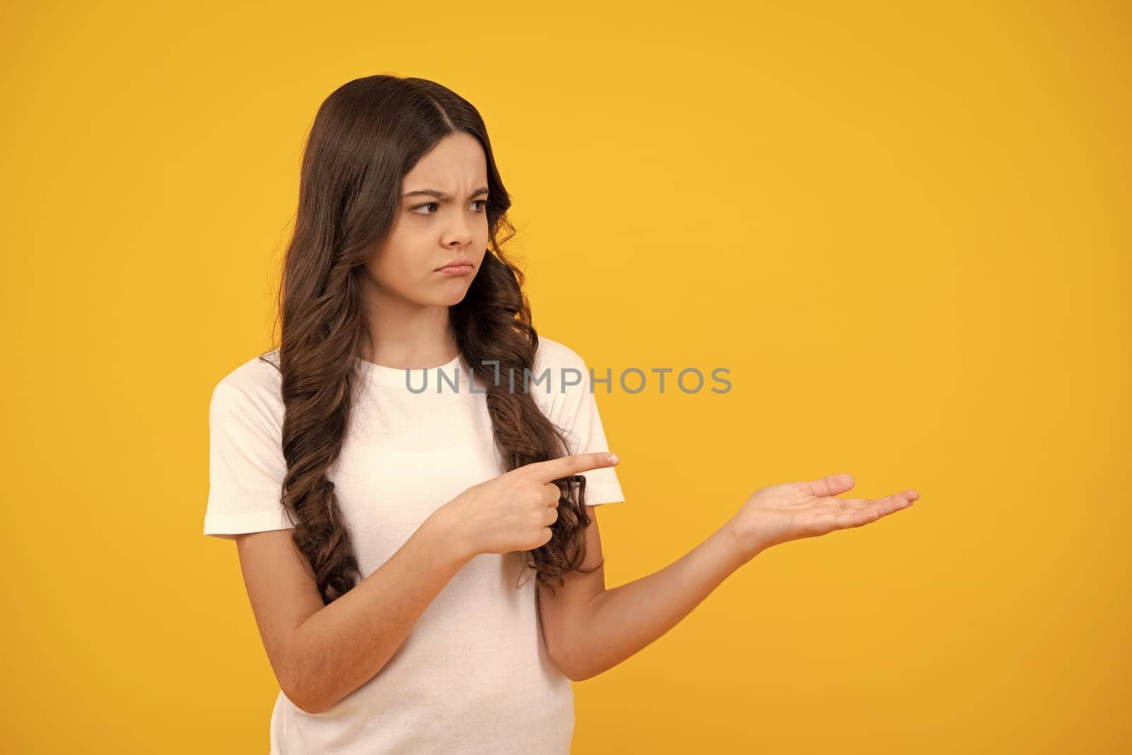 Unhappy sad teenager girl. Portrait of cute teenager child girl pointing hand showing adverts with copy space over yellow background. by RedFoxStudio