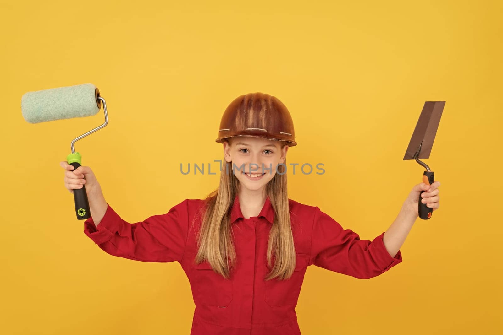 happy teen child in builder hard hat with paint roller and spatula on yellow wall by RedFoxStudio