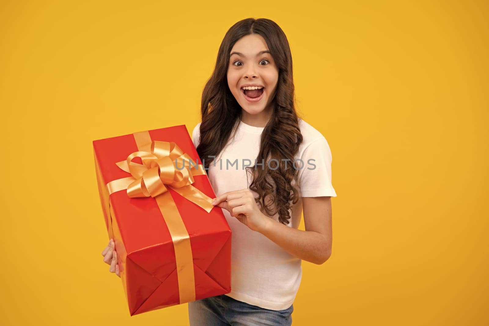 Amazed teenager. Child teen girl 12-14 years old with gift on yellow isolated background. Birthday, holiday present concept. Excited teen girl