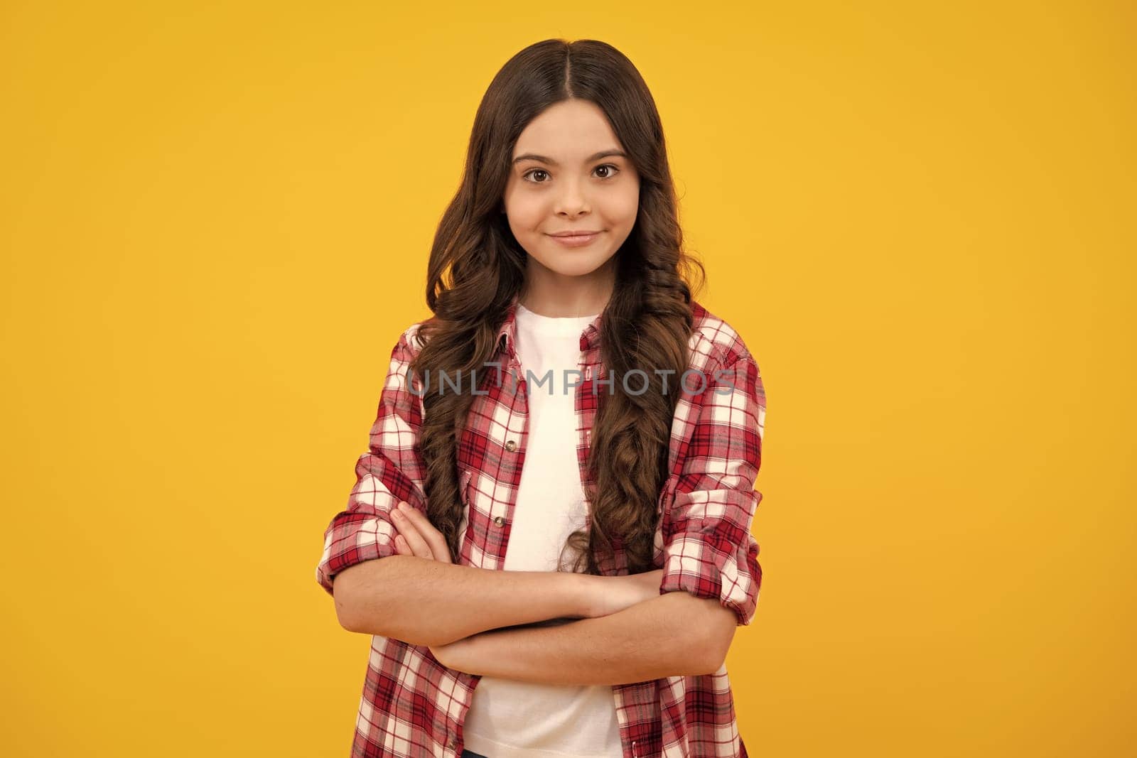 Confident child keep arms crossed, isolated on yellow background, empty space. Little caucasian teenage girl 12, 13, 14 years old hold hands crossed. Happy teenager girl