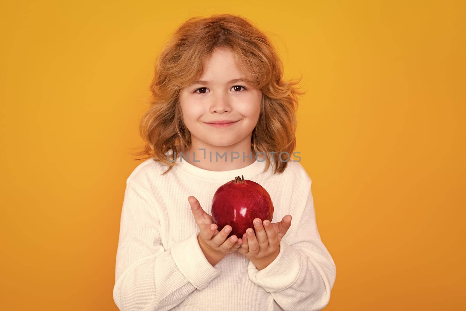 Kid hold red pomegranate in studio. Pomegranate fruit. Studio portrait of cute child with pomegranate isolated on yellow background