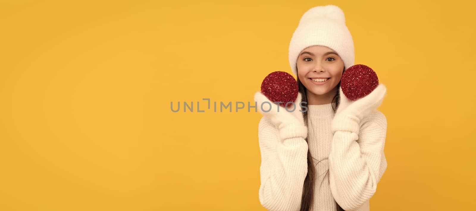 cheerful child in winter hat and gloves hold decorative xmas balls on yellow background, xmas. Banner of christmas child girl, studio kid winter portrait with copy space. by RedFoxStudio