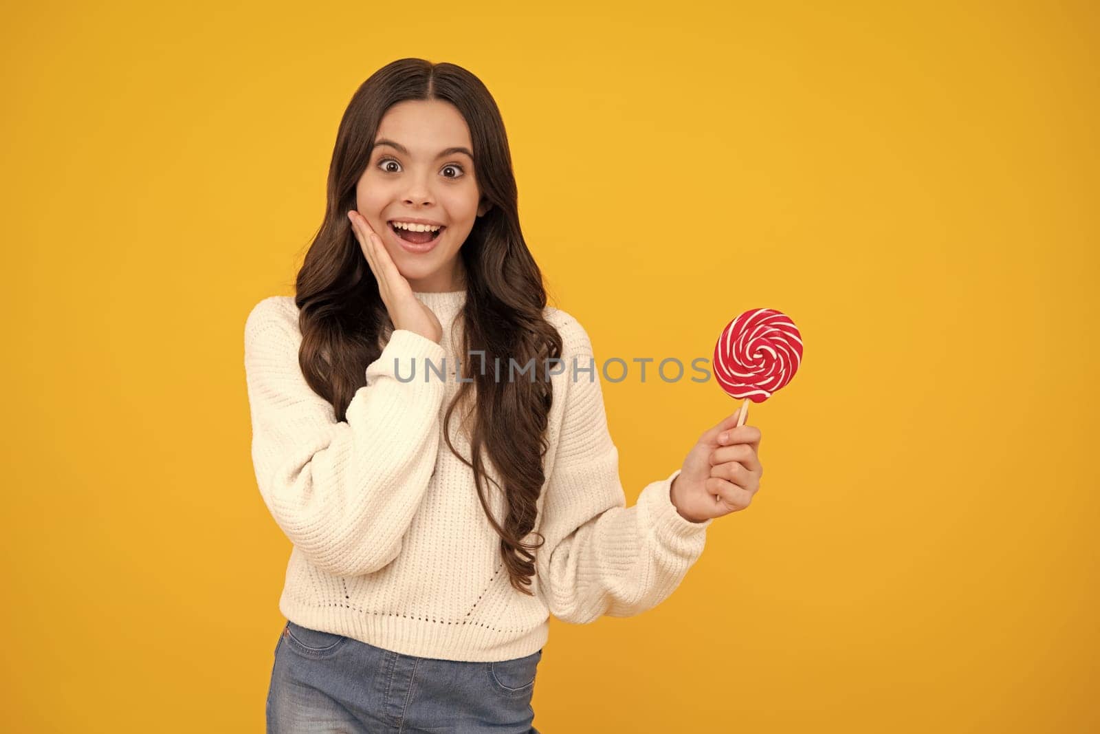 Teen girl hold lollipop caramel on yellow background, candy shop. Teenager with sweets suckers. Happy face, positive and smiling emotions of teenager girl. by RedFoxStudio