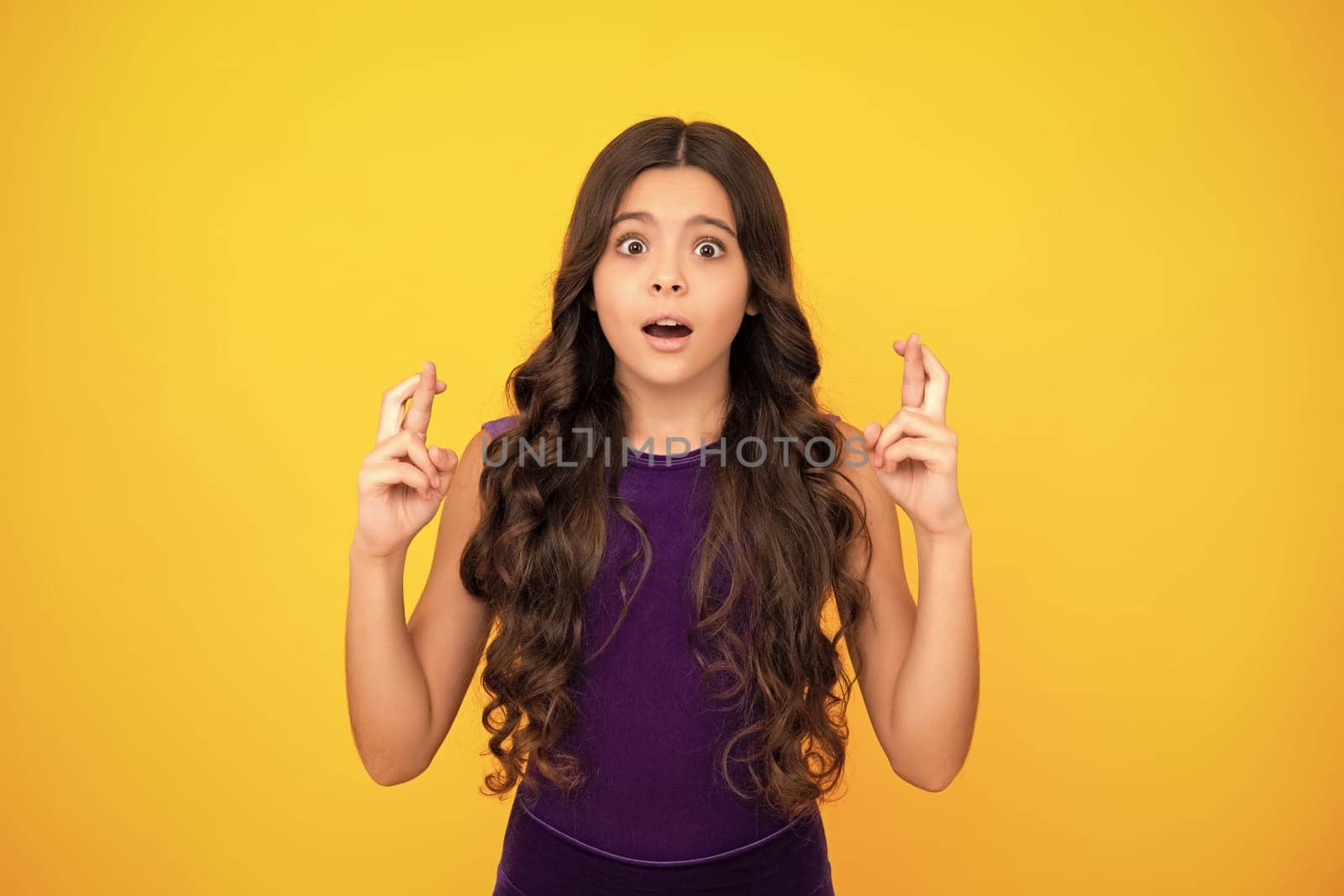 Angry teenager girl, upset and unhappy negative emotion. Glad teenager girl crosses fingers, anticipate hearing good news, isolated yellow background. by RedFoxStudio