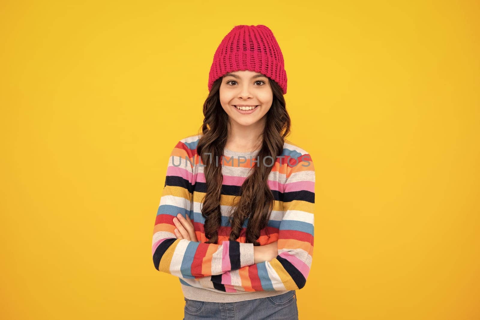 Beautiful teen girl in a winter hat and a warm sweater. A child on a yellow isolated background. Happy teenager, positive and smiling emotions of teen girl