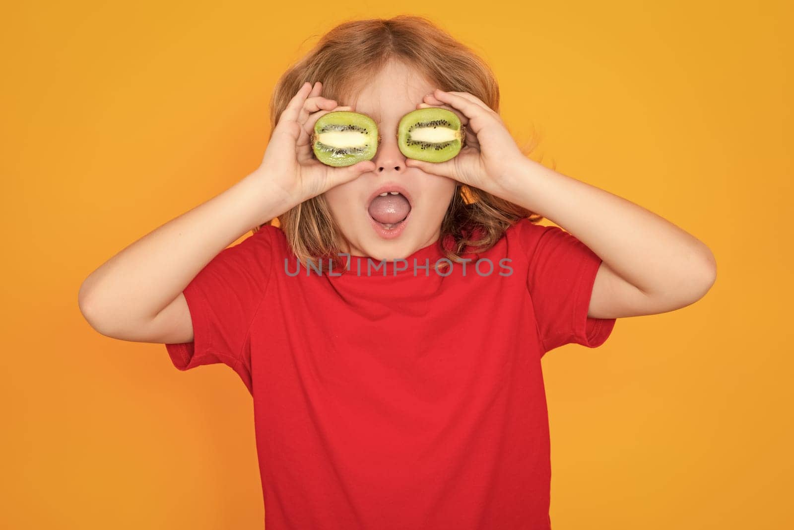 Kids face with fruits. Child hold kiwi in studio. Kiwi fruit. Studio portrait of cute kid boy with kiwi isolated on yellow. by RedFoxStudio