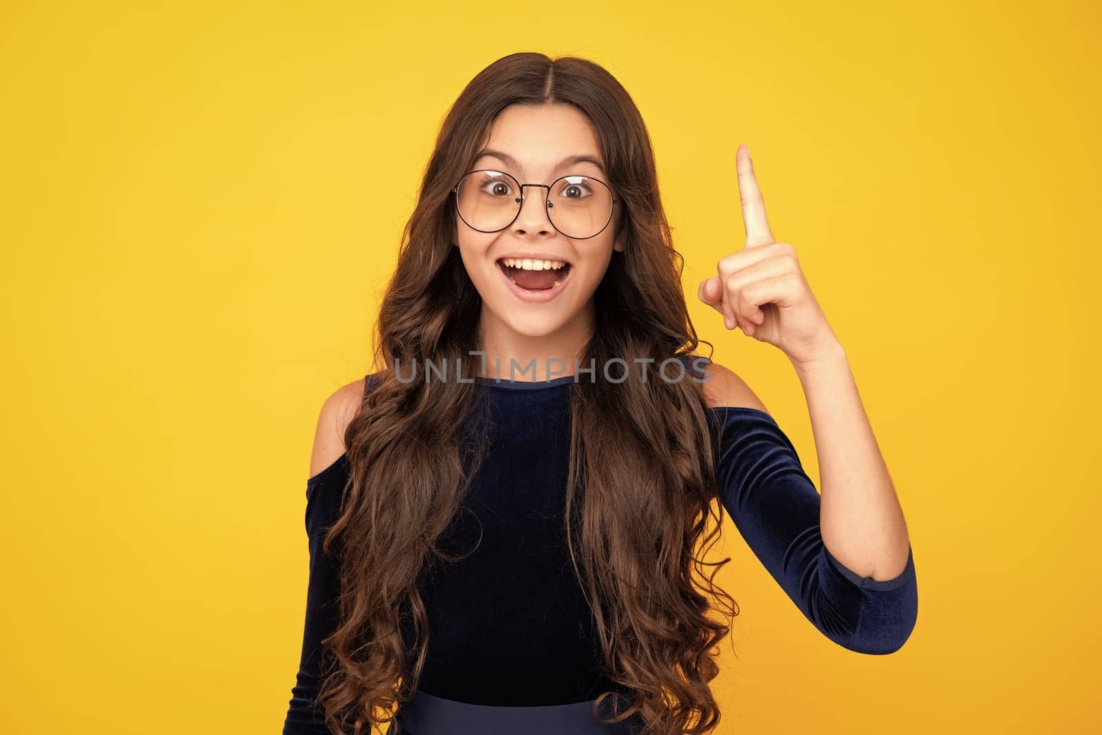 Excited teenager girl. Close up funny face of young teenager pointing up with finger, isolated on yellow background. Girl has great new idea. Successful child