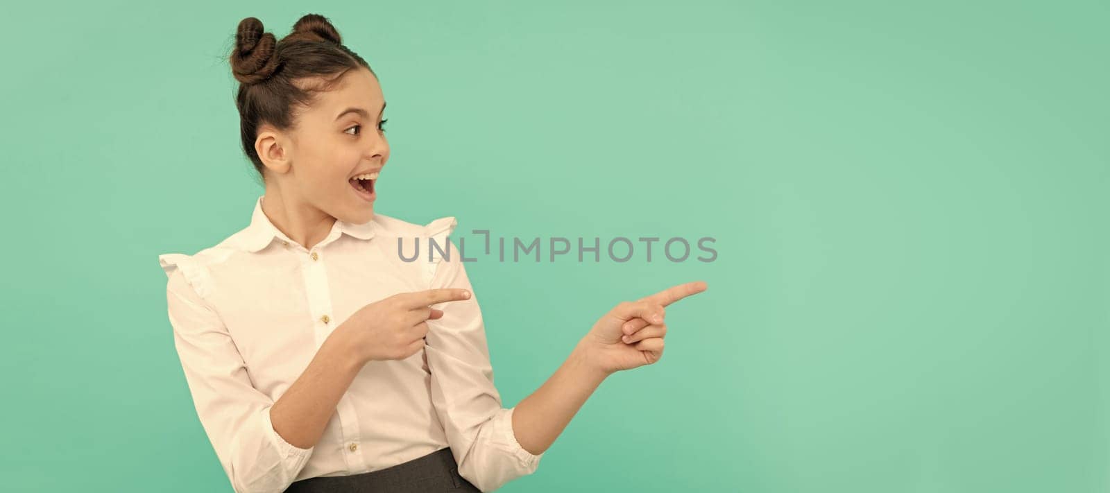 Exclusive. Happy schoolchild point fingers. Pointing gesture. Pointing for advertising. Child face, horizontal poster, teenager girl isolated portrait, banner with copy space. by RedFoxStudio