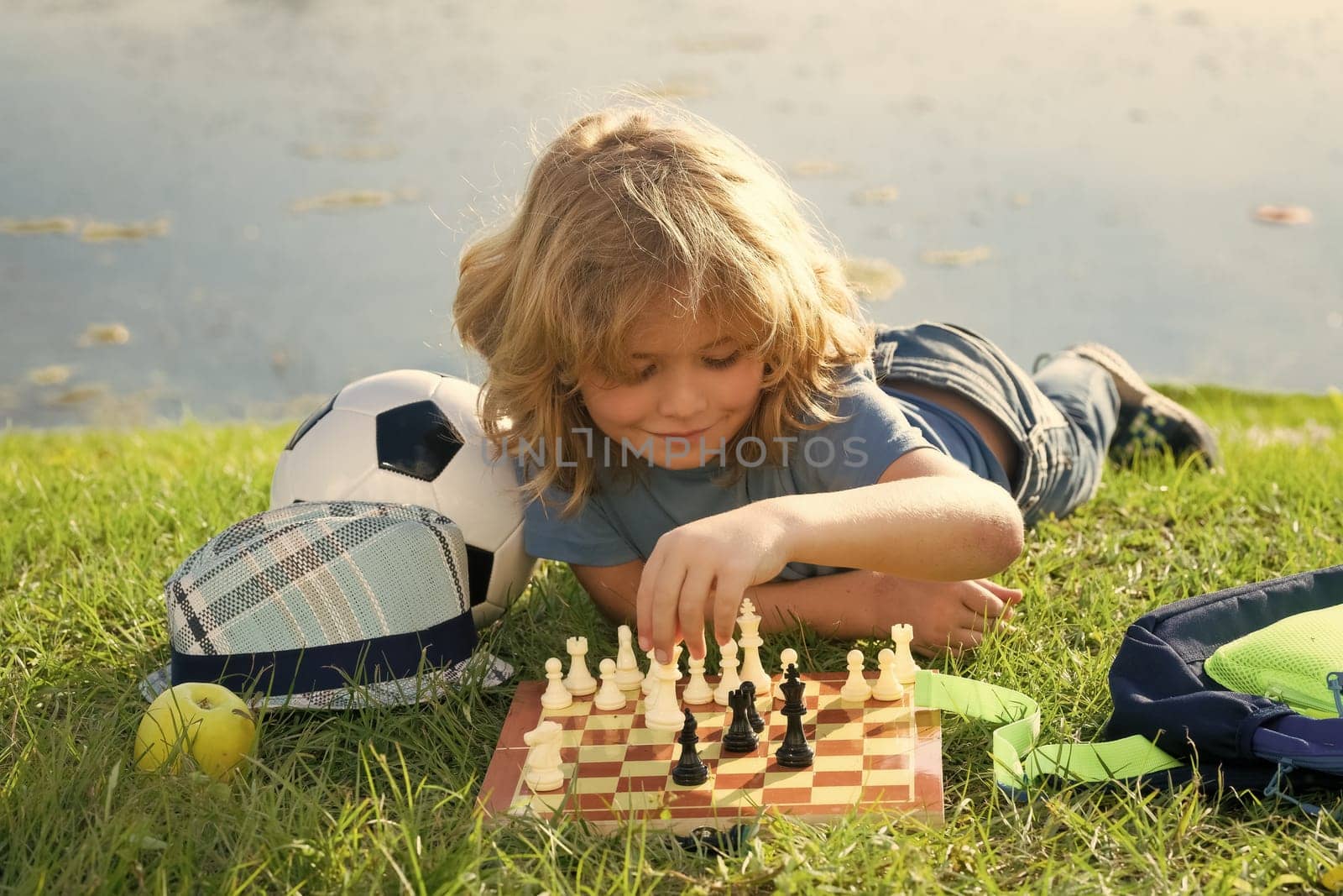 Chess school outdoor. Child think or plan about chess game, laying on grass in summer park. Intelligent, smart and clever school kids