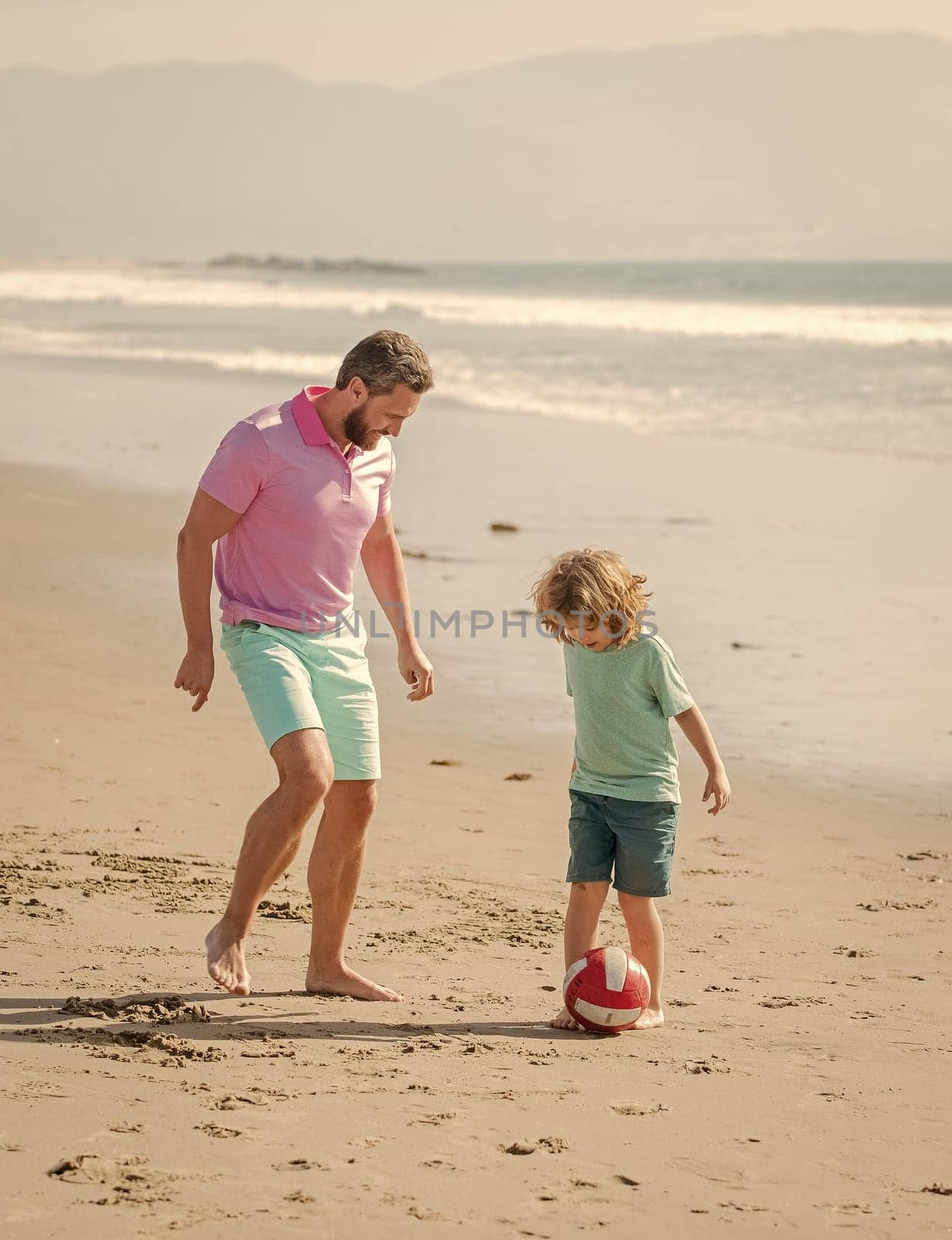 small kid and dad running on beach in summer vacation with ball, parenting.