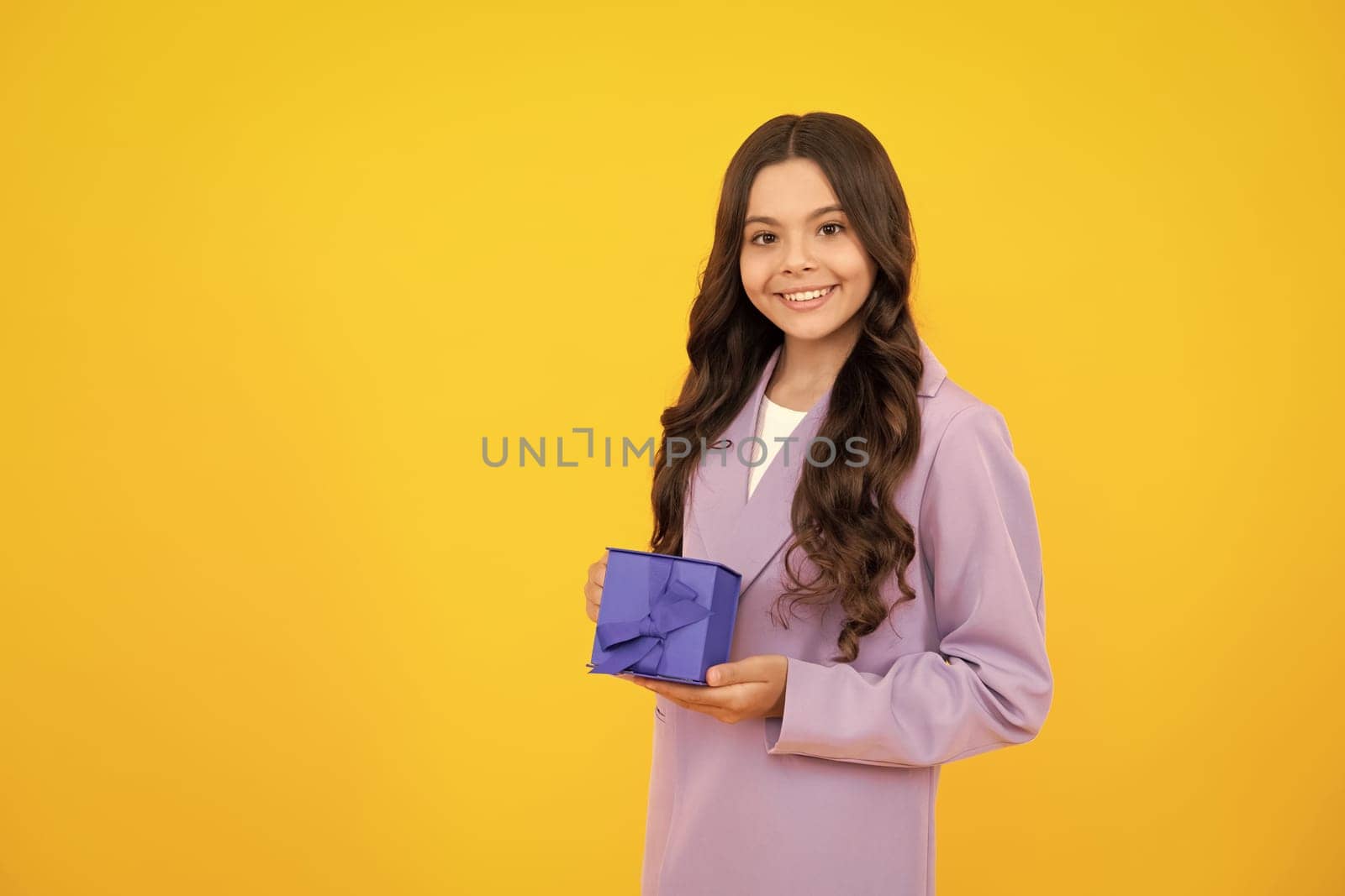 Happy teenager, positive and smiling emotions of child girl. Teenager kid with present box on isolated yellow background. Teen girl giving birthday gift. Present, greeting and gifting concept. by RedFoxStudio