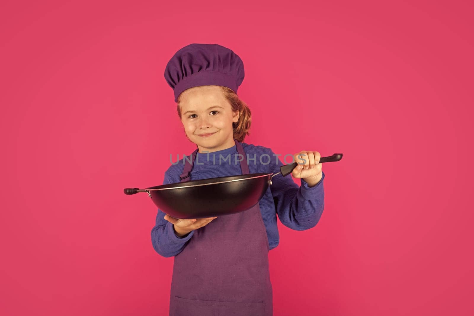 Kid cook with cooking pan. Cooking children. Chef kid boy making healthy food. Portrait of little child in chef hat isolated on studio background. Kid chef. Cooking process