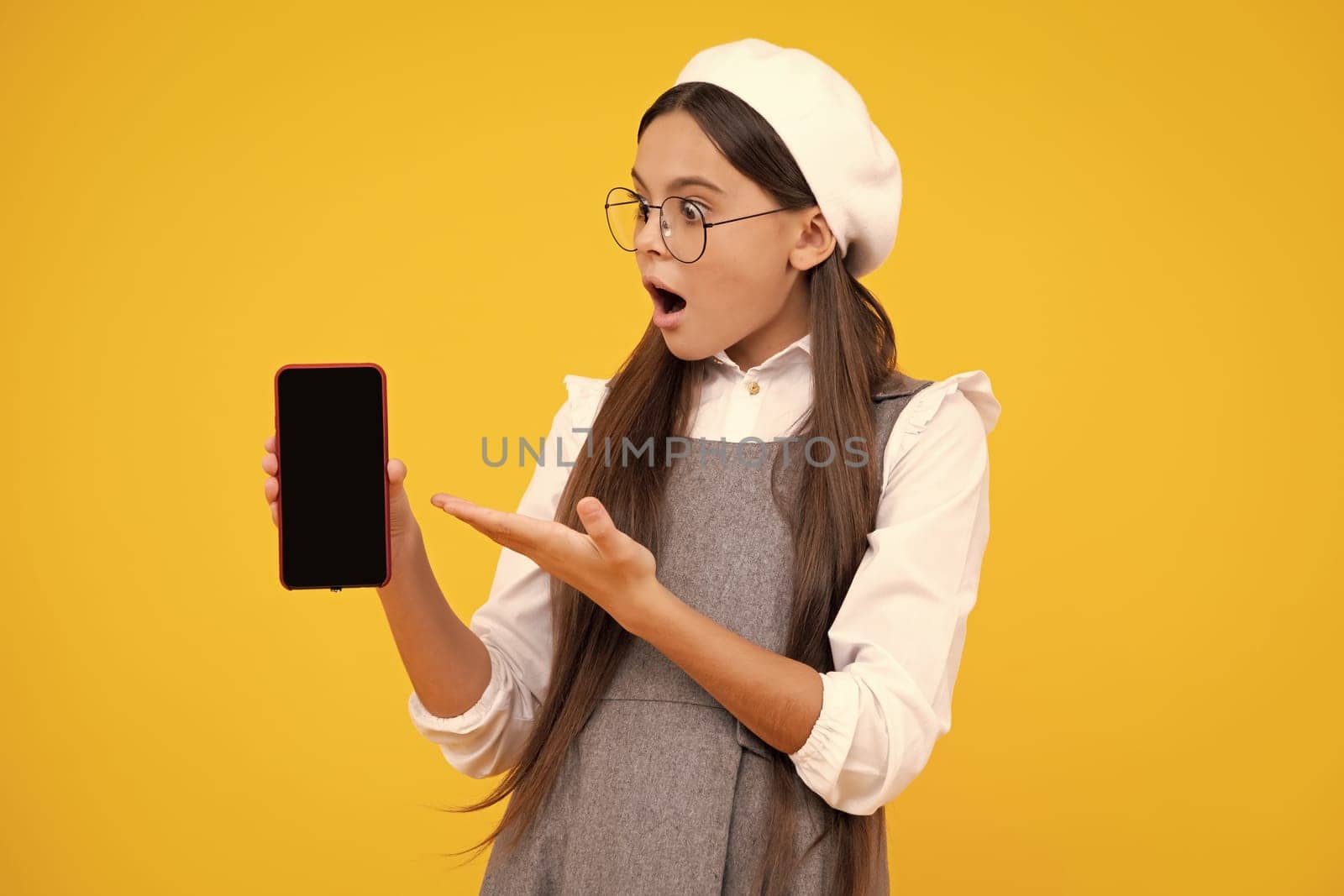 Surprised teenager girl 12, 13, 14 years old with smart phone. Hipster teen girl types message on cellphone, enjoys mobile app. Kid showing blank screen mobile phone, mock up copy space