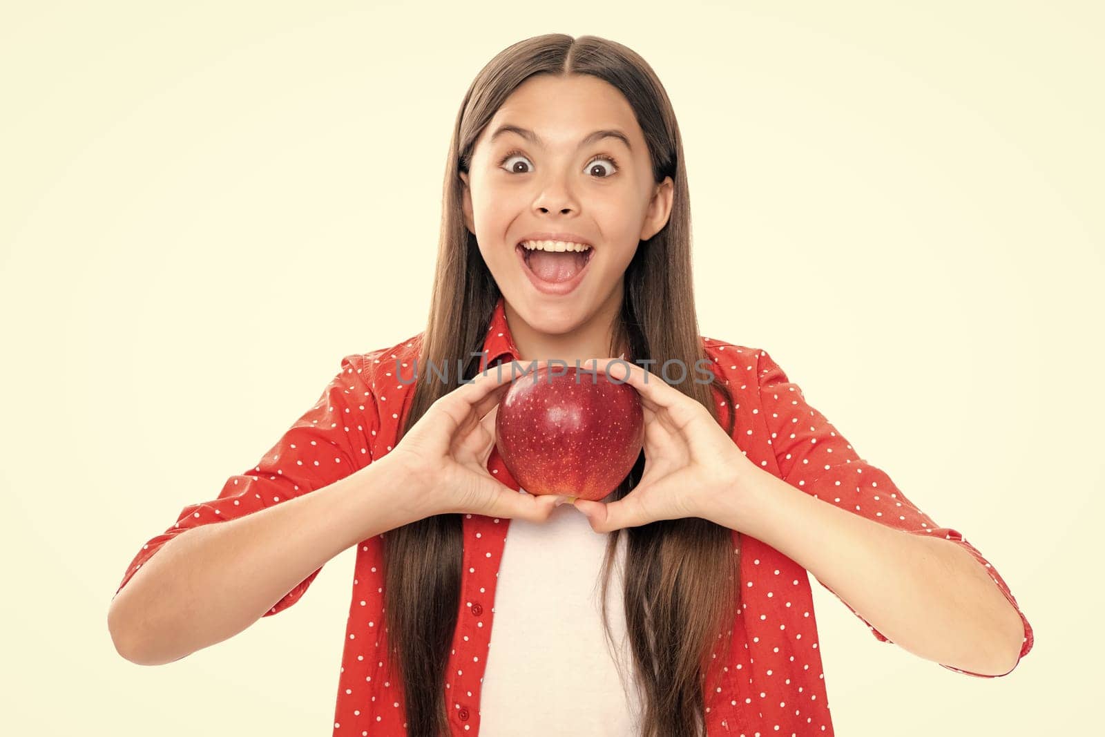 Child girl eating an apple over isolated white background. Tennager with fruit. Portrait of emotional amazed excited teen girl. by RedFoxStudio