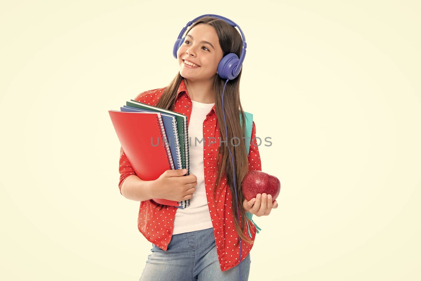 Back to school. Schoolgirl student in headphones with school bag backpack hold book on isolated studio background. School and education concept. Portrait of happy smiling teenage child girl