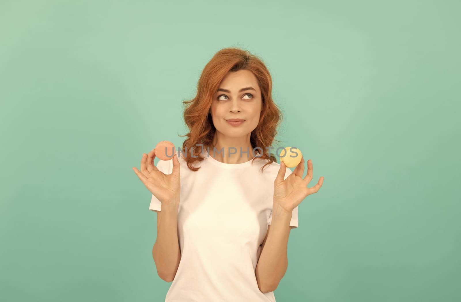 positive girl hold sweet macaron french cookie on blue background.