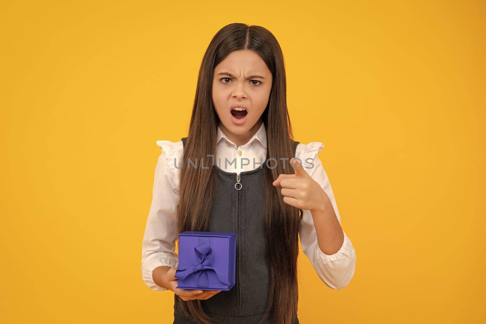 Child with gift present box on isolated studio background. Gifting for kids birthday. Unhappy upset teenager girl