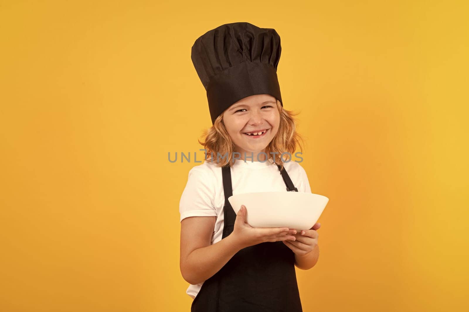 Funny child cook with cooking plate. Chef kid preparing healthy food. Portrait of child with chef hats