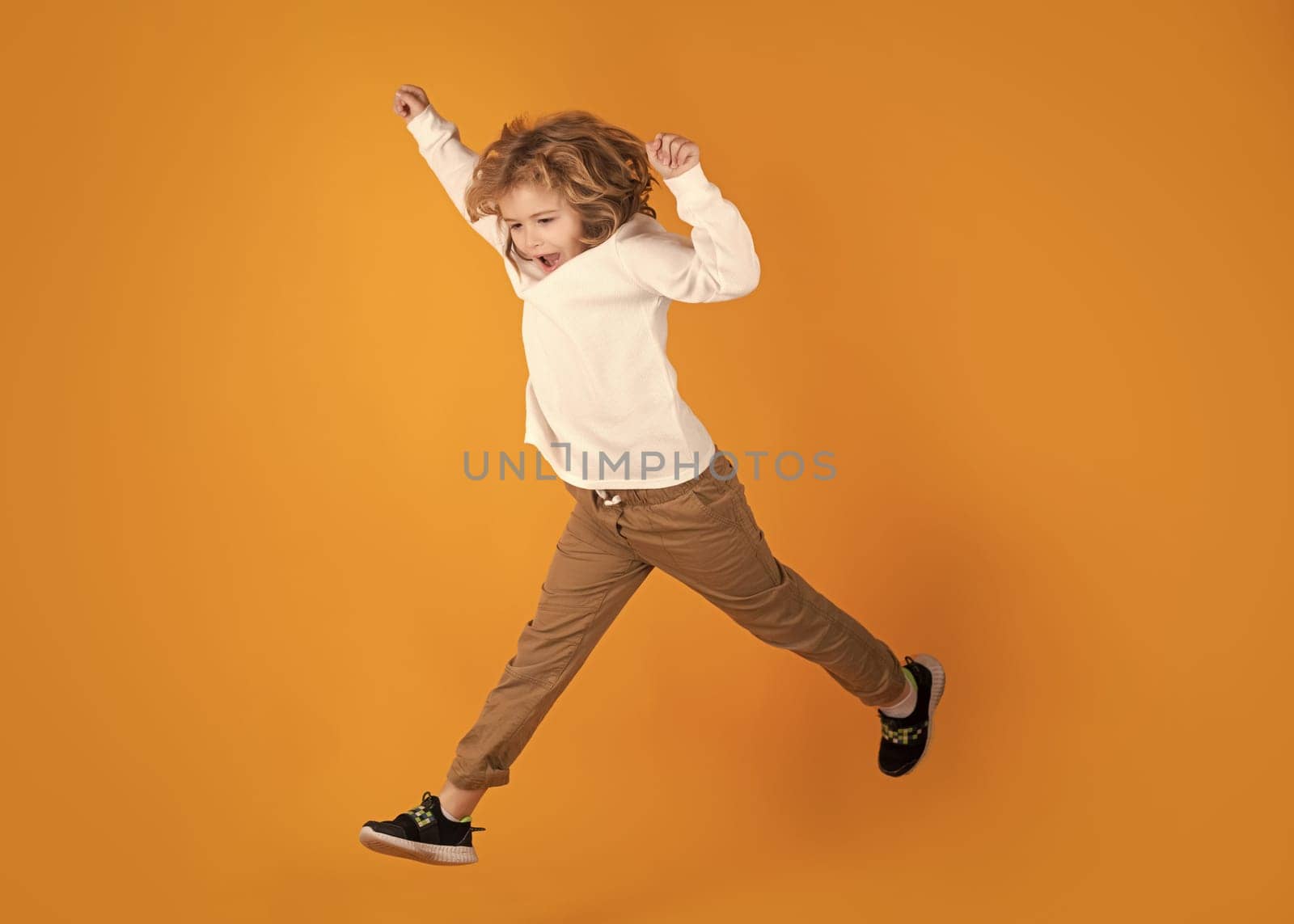Full length of excited kid jumping. Full body of little child jump wear casual t-shirt and jeans isolated on yellow background