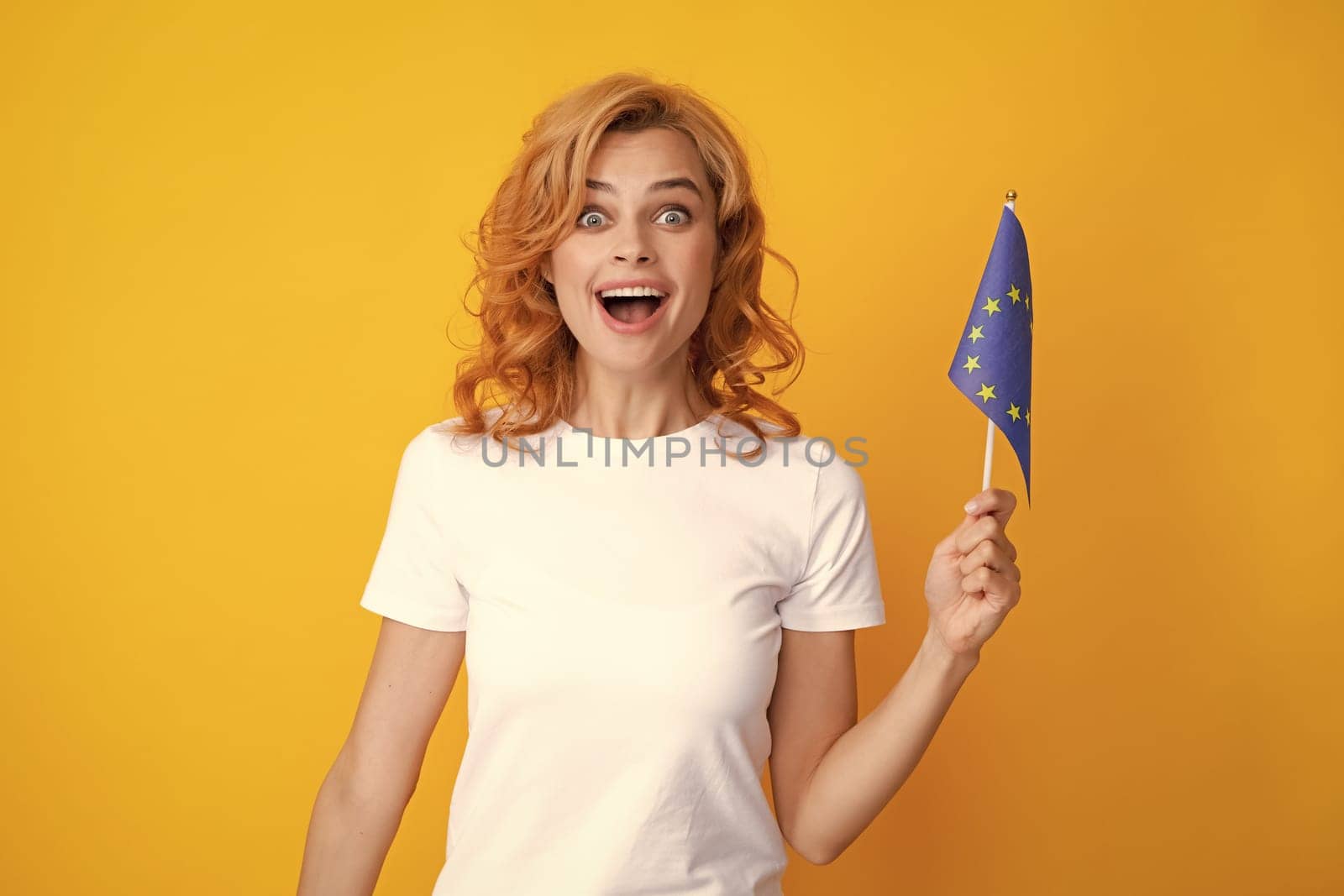 Young excited woman holding flag of europe union, isolated on yellow. EU association. Happy girl holding flag of European Union, immigration and travelling in Europe