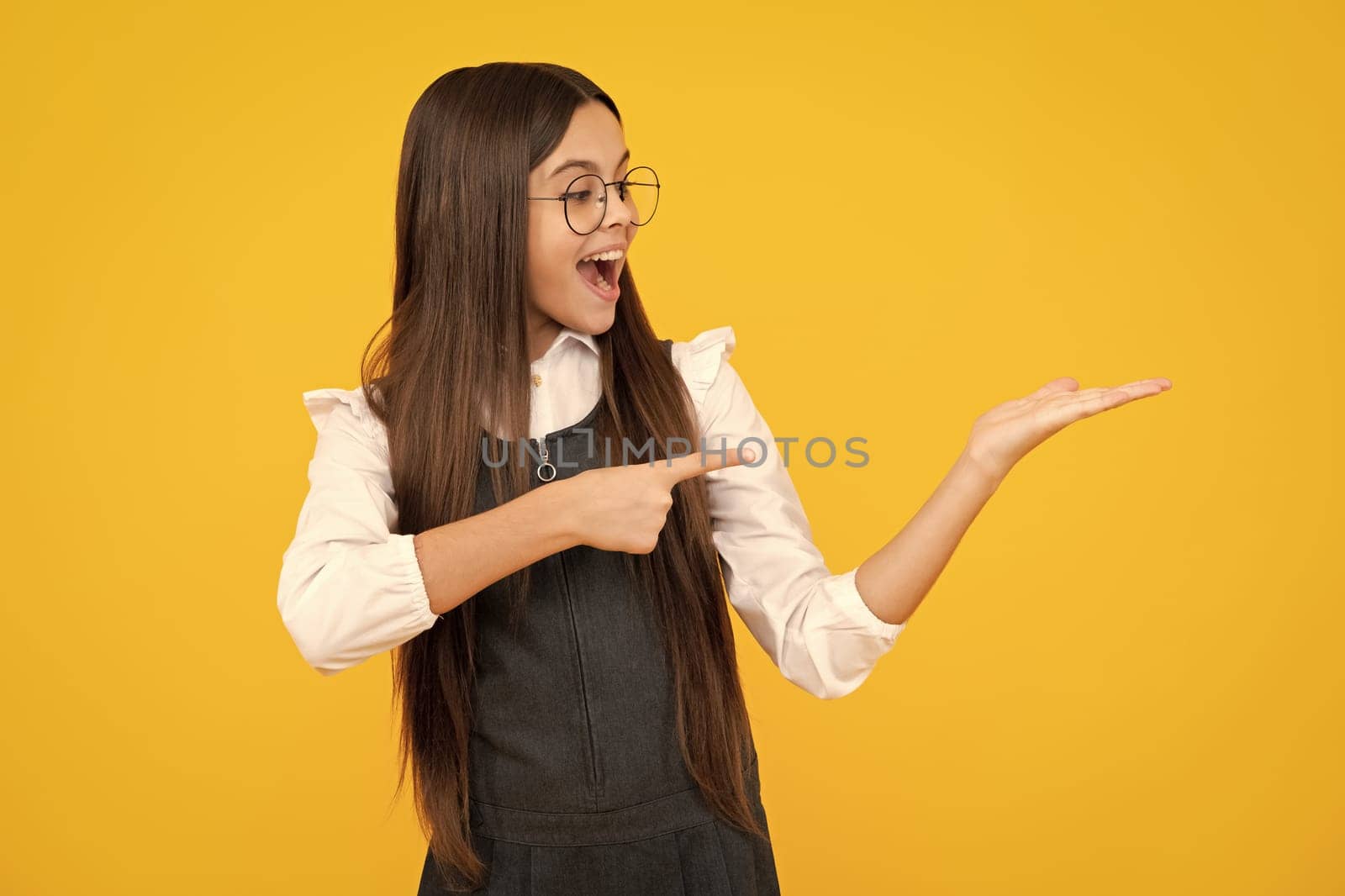 Impressed teenage girl showing recommendation copyspace. Child teenager points away, pointing aside at copy space. Excited face, cheerful emotions of teenager girl