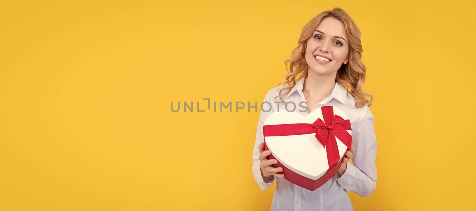 glad woman hold present heart box on yellow background. Woman isolated face portrait, banner with mock up copy space