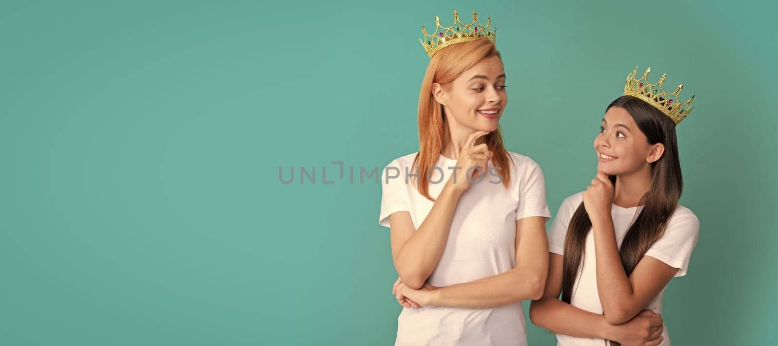 Mother and daughter child banner, copy space, isolated background. Arrogant woman mother and daughter child smile at each other wearing crowns blue background, selfish