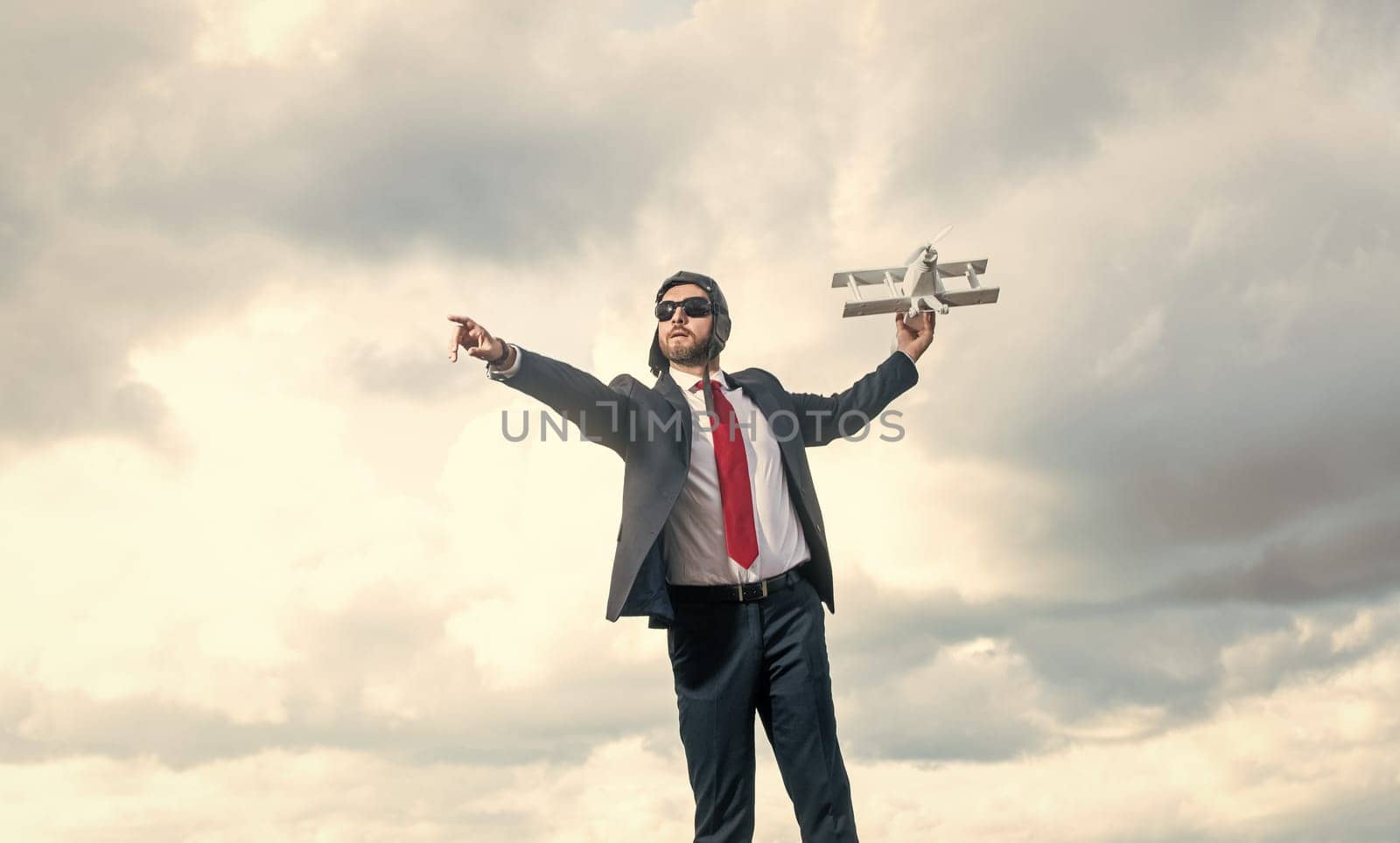 successful businessman in suit and pilot hat launch plane toy on sky background.