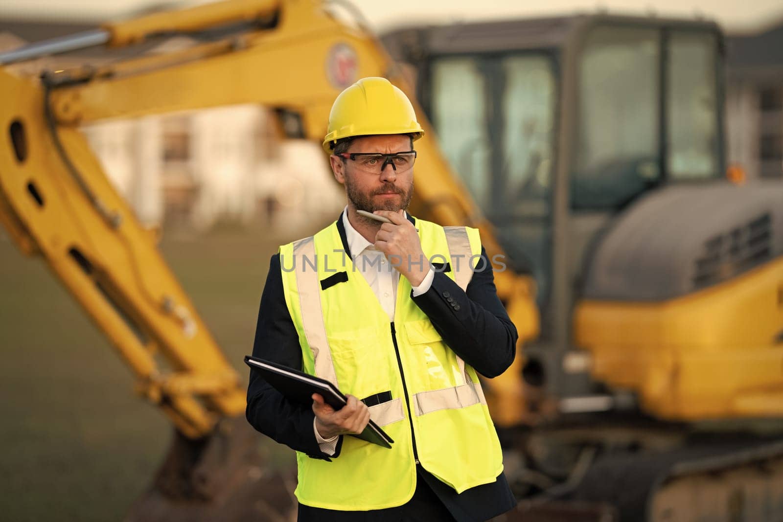 Construction manager in suit and helmet at a construction site. Construction manager worker or supervisor wearing hardhat in front of house. Supervisor construction manager near excavator. Renovation