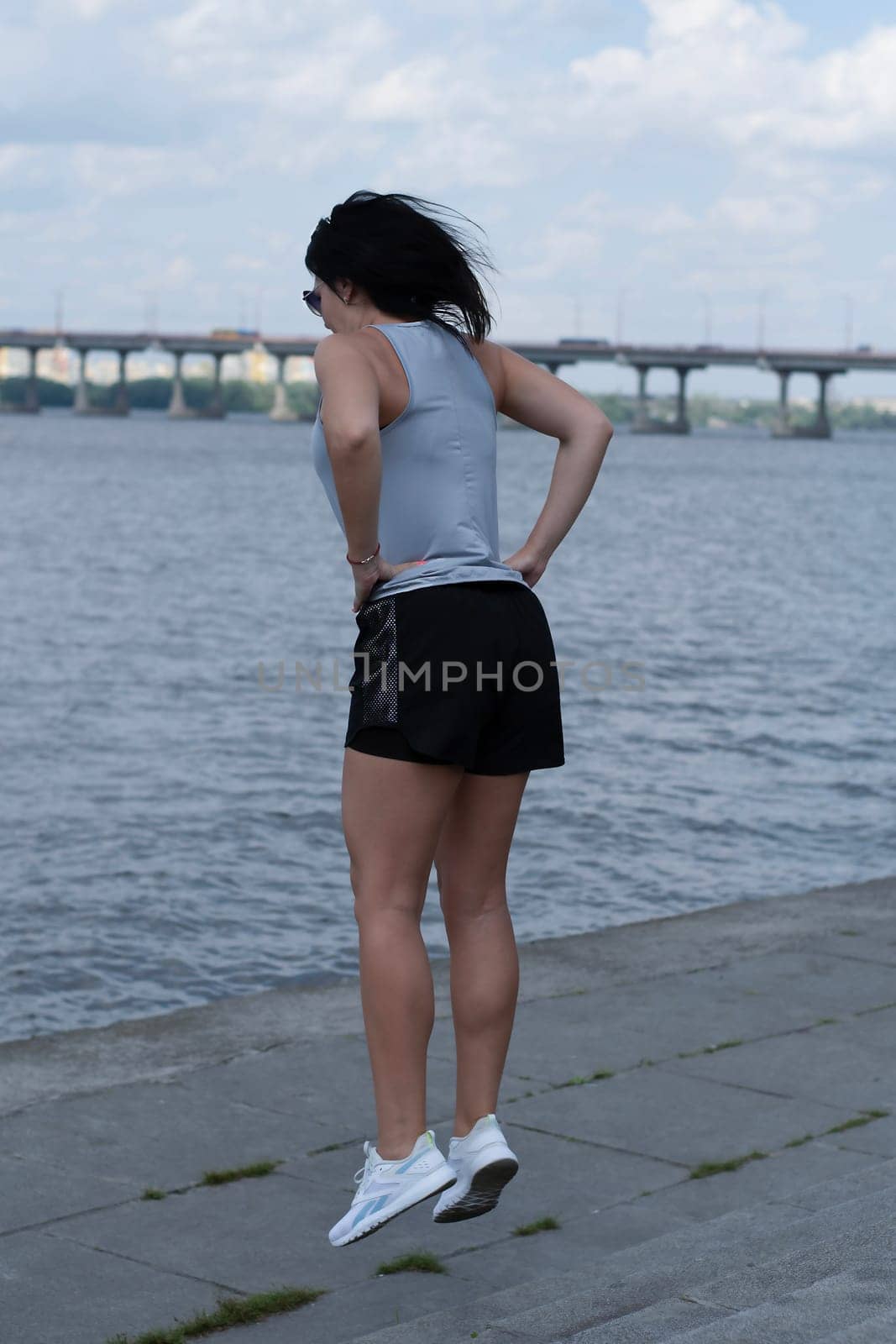 A slender and tall girl jumps on the steps on the embankment by the river. Outdoor sports. Leg workout. Fitness concept.