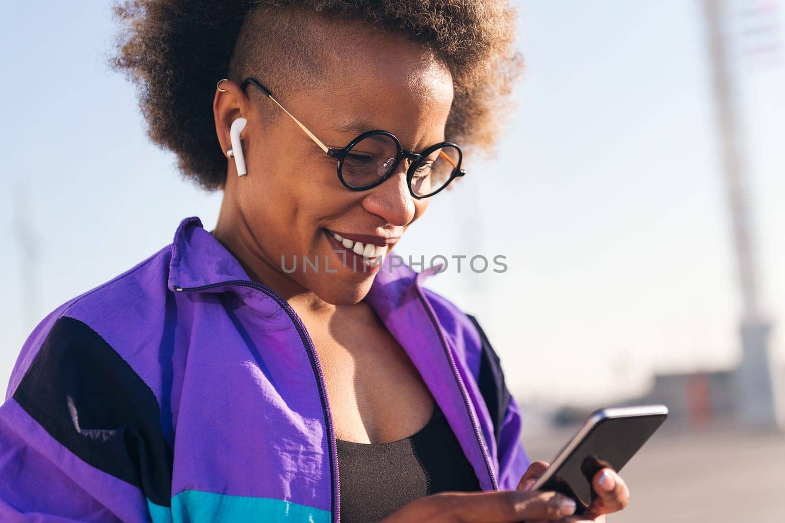 close up portrait of a cool african american female sportswoman playing music on mobile phone using earphones, concept of technology and sportive lifestyle